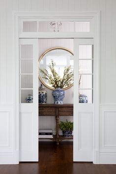 an open door leading to a room with white walls and wood floors, blue and white vases on the table