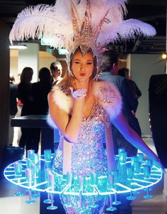 a woman in a feathered headdress is standing next to many wine glasses