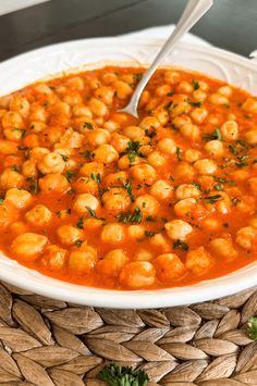 a white bowl filled with chickpeas and garnished in tomato sauce on top of a woven place mat