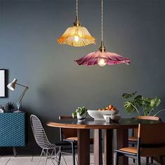 a dining room table and chairs with two hanging lights above it, next to a potted plant