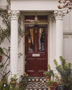 a red front door with white columns and checkerboard flooring in front of it