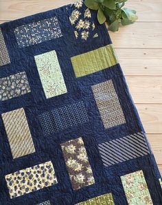 a blue quilt with green and gold squares on it next to a potted plant