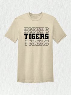 Introducing our Tigers Mascot Shirt, the perfect apparel for all the Tiger fans out there!  Whether you're a proud member of the Tigers team, a dedicated fan, or simply want to show your support, this shirt is a must-have addition to your collection. Designed with the iconic Tigers Mascot, this shirt captures the spirit and energy of your beloved team. Made with high-quality materials, this Tigers School Shirt is not only comfortable but durable as well. You'll love the softness of the fabric ag Fan Apparel T-shirt With Letter Print, College Fan Apparel T-shirt With Team Name, School Spirit Short Sleeve T-shirt With Letter Print, Graphic Print Crew Neck T-shirt For Fans, Team Spirit Streetwear T-shirt, Pre-shrunk Team Spirit T-shirt For Streetwear, Pre-shrunk Team-colored Fan Apparel T-shirt, School Spirit Graphic T-shirt Fan Gear, School Spirit Graphic T-shirt For Fan Gear