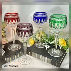 three wine goblets sitting on top of two books next to flowers and greenery