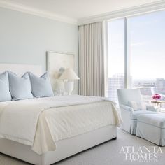 a white bed sitting in a bedroom next to a tall window with curtains on it