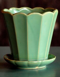 a green vase sitting on top of a table next to a cup and saucer