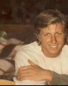 a man is smiling and holding something in his right hand while sitting on a bed