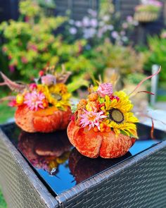 two orange pumpkins with flowers on them sitting on a table in front of some plants