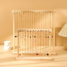 a wooden jewelry rack with lots of necklaces hanging from it's sides on a table next to a lamp