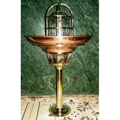 a brass candle holder with a birdcage on the top and a green marble wall behind it