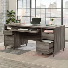 an office desk with a laptop on it in front of a window and a rug