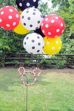 a bunch of balloons that are on top of a pole in the grass with a heart