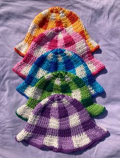 four crocheted hats are lined up on a purple sheet with white and green stripes