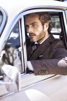 a man in a suit and tie is sitting in a car looking out the window