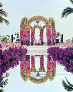 an outdoor wedding setup with purple flowers and greenery on the ground, surrounded by palm trees