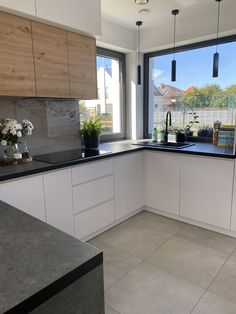 a kitchen with white cabinets and black counter tops next to a large window that looks out onto the backyard