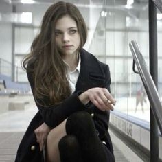 a woman sitting on an escalator with her legs crossed and looking at the camera