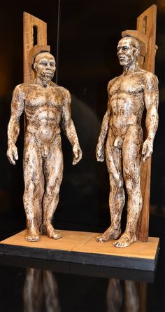 two statues of men standing next to each other in front of a black wall and mirror