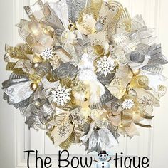 the bowtiquee wreath is decorated with gold, silver and white ribbon bows on it