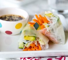 a white plate topped with vegetable rolls next to a bowl of soup