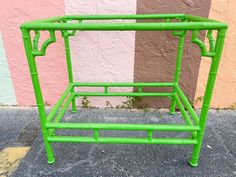 a green metal rack sitting on the side of a road next to a pink wall