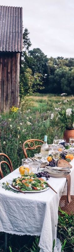 an outdoor table set up with plates and bowls on it in the middle of a field