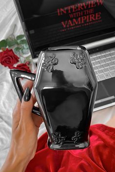 a woman is holding a black vase in front of a laptop on a red blanket