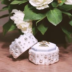 two wedding rings sitting on top of a box next to white flowers and greenery