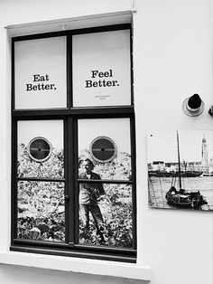 a black and white photo of a man looking out the window at boats in the water