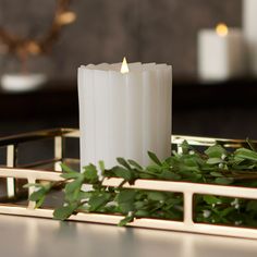 a white candle sitting on top of a table next to some greenery and candles