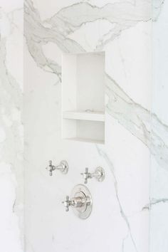 a bathroom with white marble walls and floor, two faucets on the wall