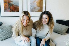 two women sitting on a couch smiling for the camera