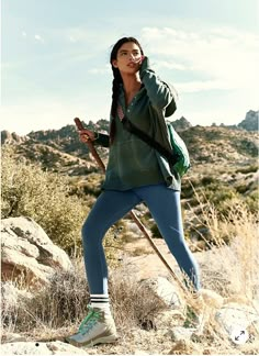 a woman standing on top of a rocky hill holding a cell phone up to her ear