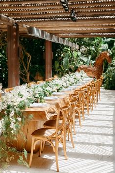 a long wooden table with white flowers and greenery on the top is surrounded by chairs