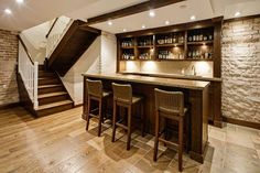 a bar with three stools in front of it next to a brick wall and stairs