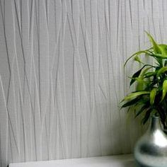 a green plant in a silver vase next to a white wall with wavy lines on it