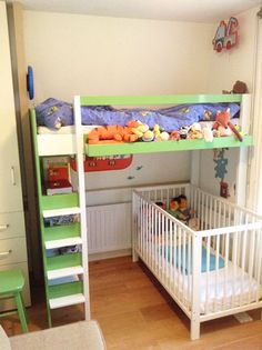 a green bunk bed sitting next to a white crib with stuffed animals on it