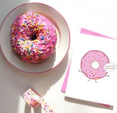 a pink donut with sprinkles sits on a plate next to a greeting card