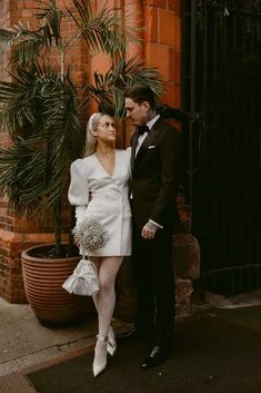 a man and woman standing next to each other in front of a building with palm trees