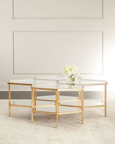 a glass and gold coffee table on carpeted floor with white flowers in the center