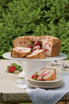 a cake with strawberries on it sitting on top of a table next to plates