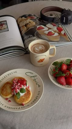 two plates with pastries and strawberries sit on a table next to an open book