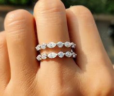 a woman's hand with two wedding rings on top of her finger, and the ring has three pear shaped diamonds