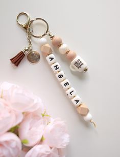 two keychains with words on them sitting next to pink flowers and a coin