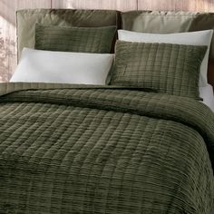 a bed with green bedspread and pillows on top of it, in front of a wooden headboard