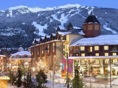 the resort is lit up at night with christmas lights on trees and snow covered mountains in the background