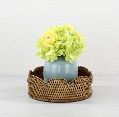 a vase with yellow flowers in it sitting on a wicker basket next to a white wall