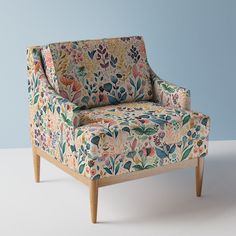 an upholstered chair with floral fabric on the back and arms, against a blue wall