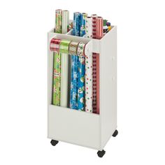 a white book rack with many books on wheels and wrapping paper in the bottom section