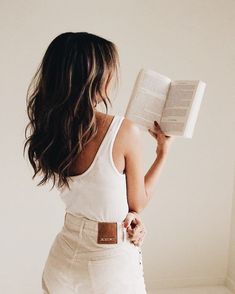 a woman is holding an open book in her right hand and looking down at the floor